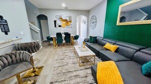A modern living room with a sofa, armchairs, a coffee table, and a dining area with chairs and a table.
