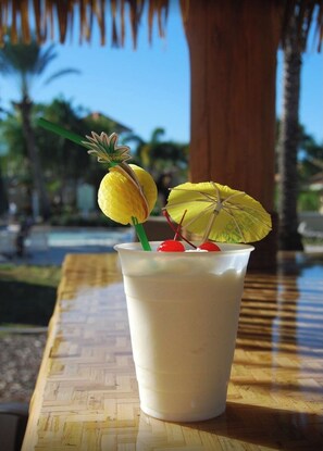 Un vaso de una bebida cremosa con una rodaja de piña y una cereza sobre una mesa de madera al aire libre.