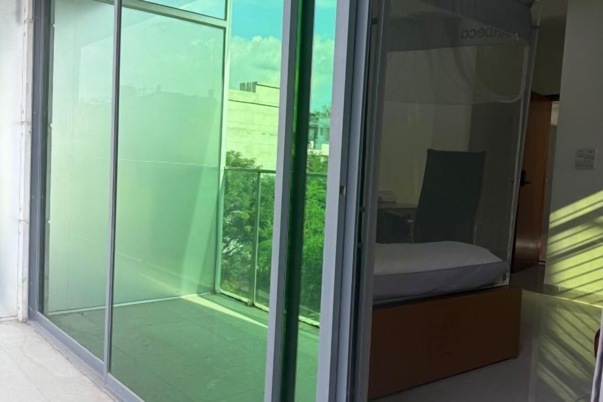 A room with a sliding glass door leading to a balcony, a bed with a mattress and pillows, and a small table.