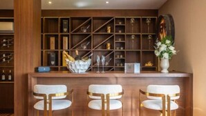 A bar area with three white bar stools and a shelf with various items.