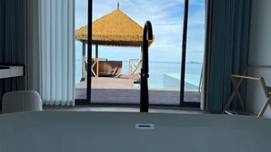 Ein Zimmer mit einer großen Glasschiebetür, die zu einem Poolbereich mit einem Reetdachschirm und Liegestühlen führt.