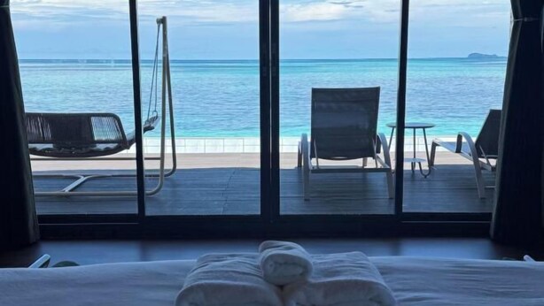 A hotel room with a bed, two towels, a view of the ocean, and a deck with chairs and a table. - Moana Water Village Semporna (Semporna)