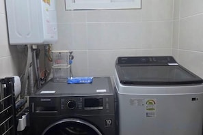 A laundry room with a Samsung washer and dryer, a water heater, and a metal rack. - JeJuHahastay (Jeju)