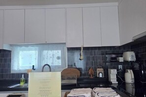 A modern kitchen with white cabinets, a black countertop, and a window with a view. - JeJuHahastay (Jeju)