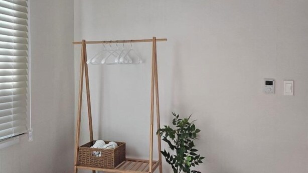 Una habitación con un perchero de madera, una cesta de mimbre, una planta en maceta y un reloj de pared.