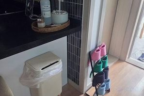 A kitchen area with a trash bin, a basket with kitchen items, and a rack with shoes. - JeJuHahastay (Jeju)