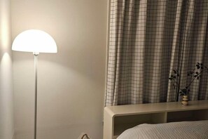 Een slaapkamer met een bed, nachtkastje, lamp en gordijn.
