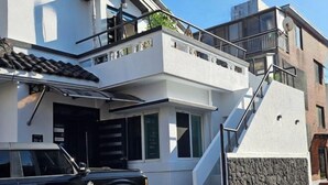 Un moderno edificio de dos pisos con un balcón, una escalera y un coche estacionado adelante.