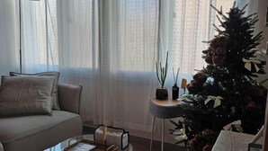 Una sala de estar con un sofá, una mesa de centro de vidrio, una mesita de noche con una planta y un árbol de Navidad.