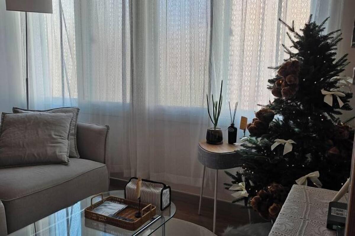 Ein Wohnzimmer mit einer Couch, einem Glastisch, einem Beistelltisch mit Pflanze und einem Weihnachtsbaum.