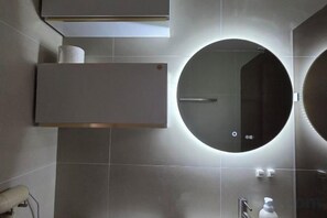 A modern bathroom with a round mirror, a towel rack, and a toilet paper holder. - JeJuHahastay (Jeju)
