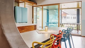 A modern dining area with a wooden table, colorful chairs, and a view of the outdoors through large glass doors. - Beyand Private Pool Villa Pension, Daebu (Ansan)