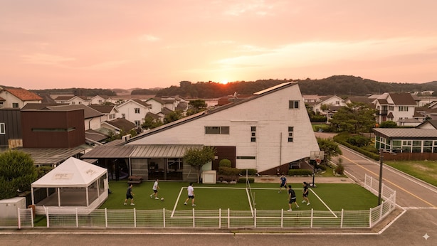 A residential area with houses, a sports field, and a building with a unique triangular roof. - Beyand Private Pool Villa Pension, Daebu (Ansan)