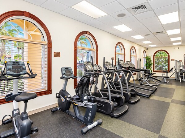 A gym with multiple treadmills, ellipticals, and exercise bikes arranged in rows.