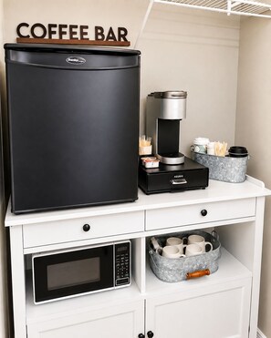 A kitchenette with a coffee maker, a microwave, and a storage bin with cups.
