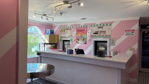 Interno di una gelateria a righe rosa e bianche, con bancone, cartelli con il menù e vista sulla finestra.