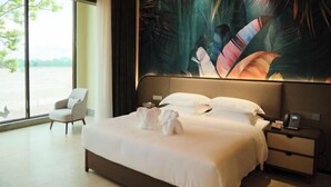 Una habitación de hotel moderna con una cama grande, una mesita de noche, una silla y vistas al exterior.