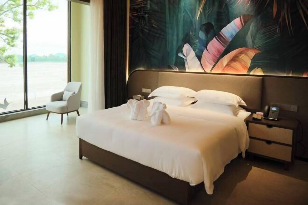 A modern hotel room with a large bed, a bedside table, a chair, and a view of the outdoors.