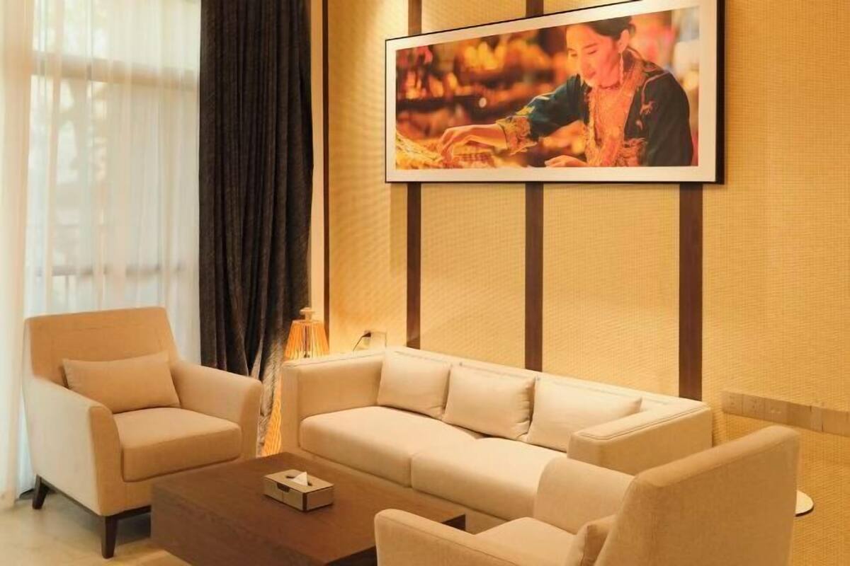 A modern living room with a beige sofa, two armchairs, and a coffee table. A framed photo is displayed on the wall above the sofa.