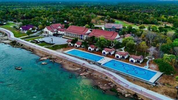 Vista aérea de un complejo turístico con una gran piscina, varias edificaciones y un paisaje circundante.