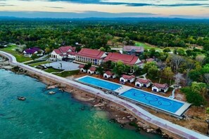 Vue aérienne d’un complexe hôtelier doté d’une grande piscine, de plusieurs bâtiments et d’un paysage environnant.