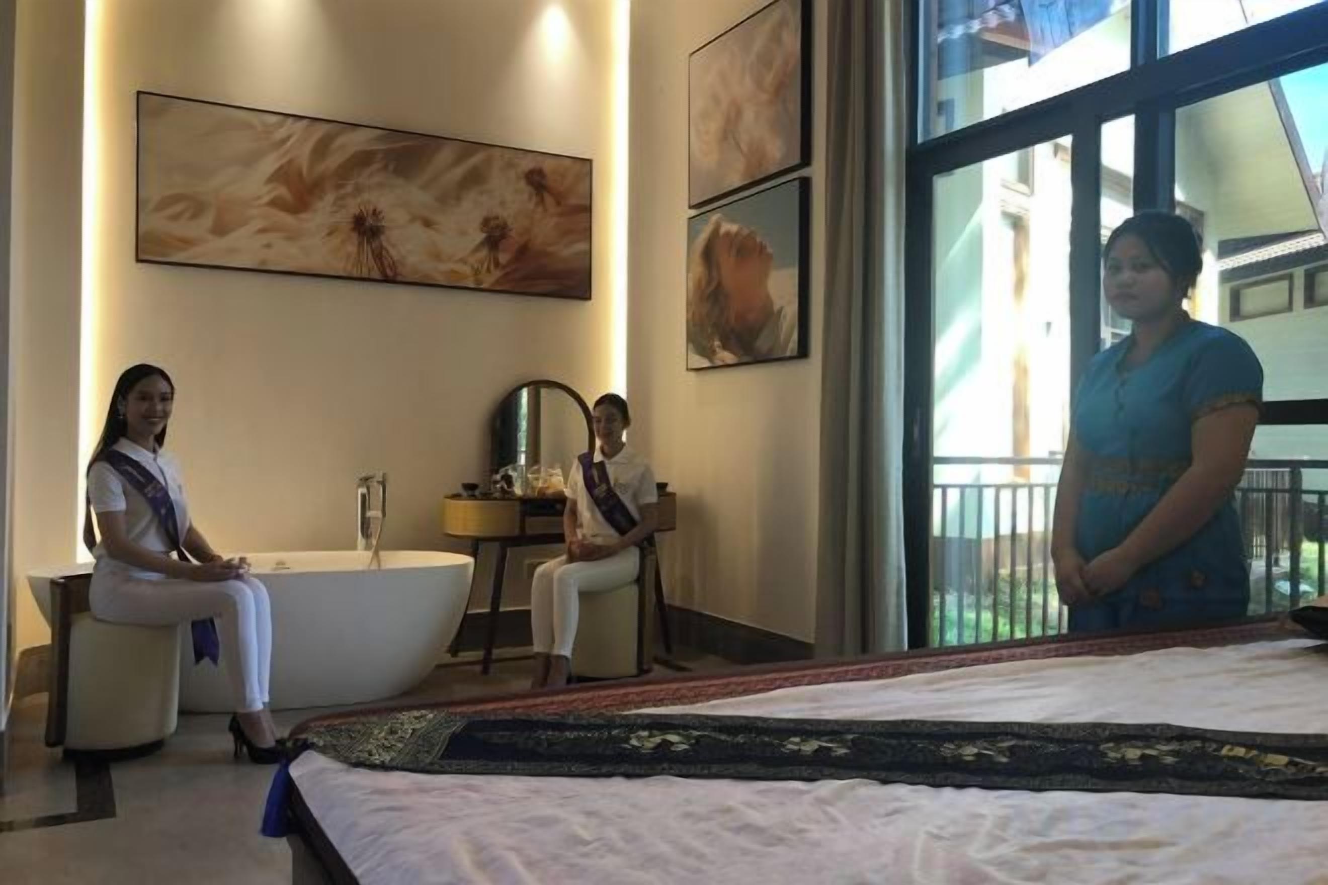 A hotel room with a bathtub, a bed, and a large window.