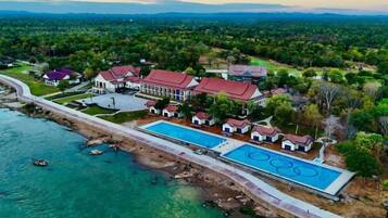 An aerial view of a resort with a large swimming pool, multiple buildings, and a coastline.