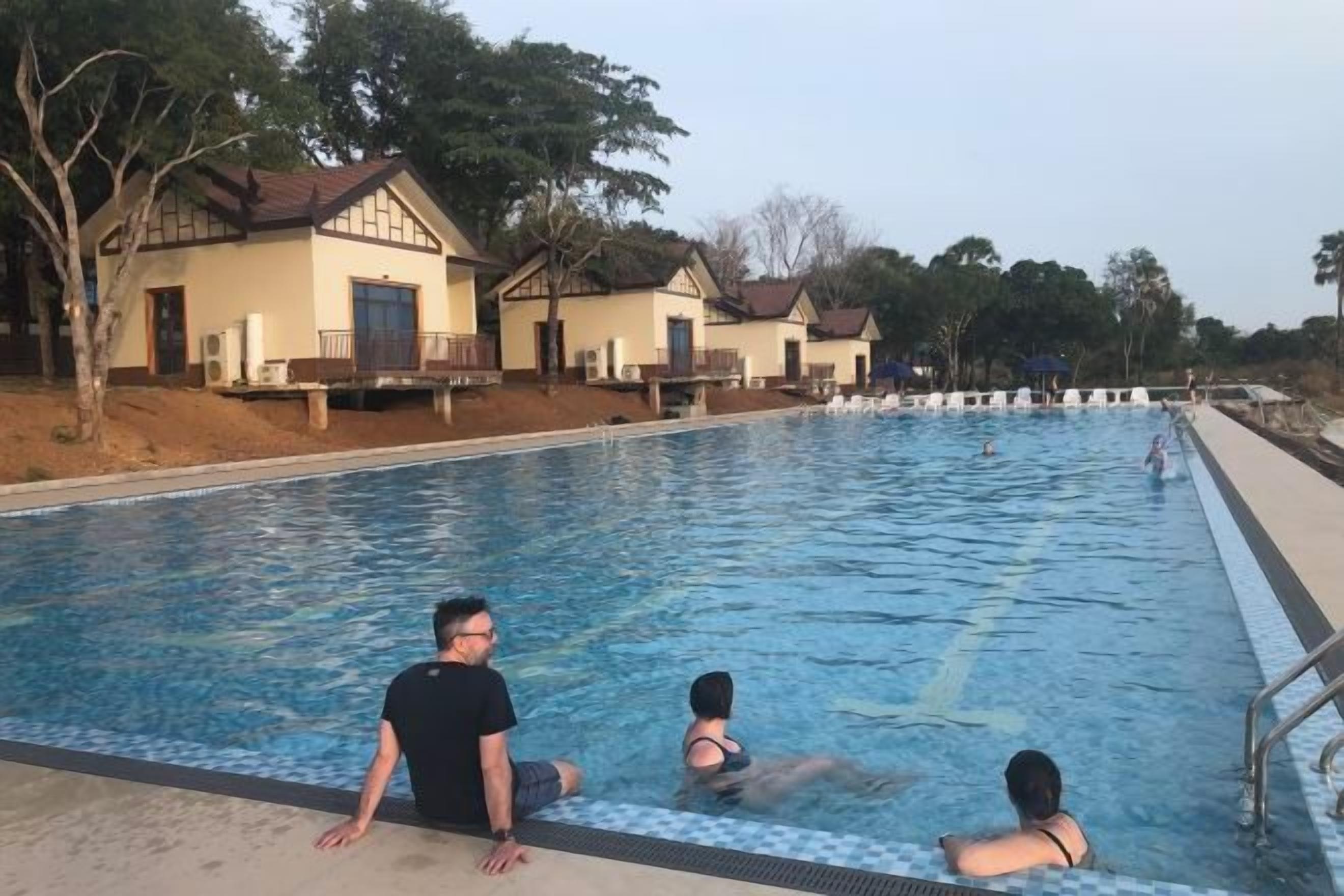 Une piscine avec une personne assise au bord, une autre personne dans l’eau et une troisième personne à l’arrière-plan.