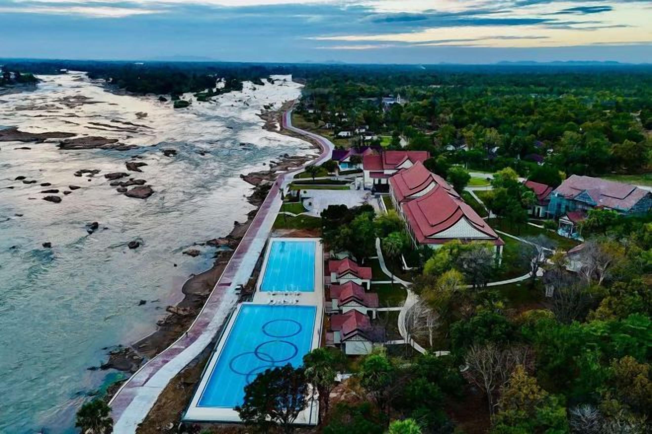 An aerial view of a coastal resort with a swimming pool, beachfront, and traditional architecture.