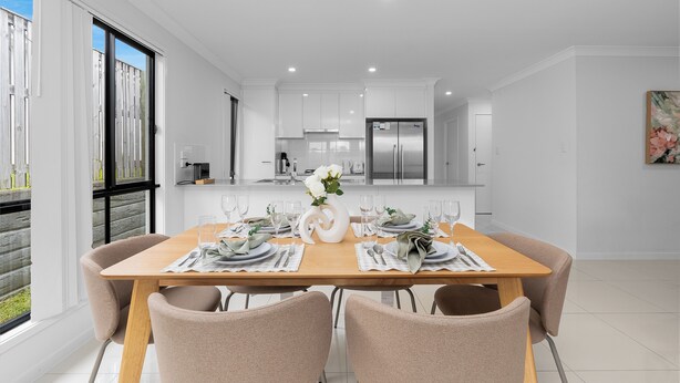 A modern dining area with a wooden table set for six, white walls, and a kitchen in the background. - Whispering Pines - Stylish 3BR Duplex close to M1 (Pimpama)