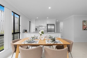 Un comedor moderno con una mesa de madera dispuesta para seis comensales, paredes blancas y una cocina al fondo.