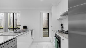 A modern kitchen with white cabinetry, stainless steel appliances, and a large window providing a view of the outdoors. - Whispering Pines - Stylish 3BR Duplex close to M1 (Pimpama)