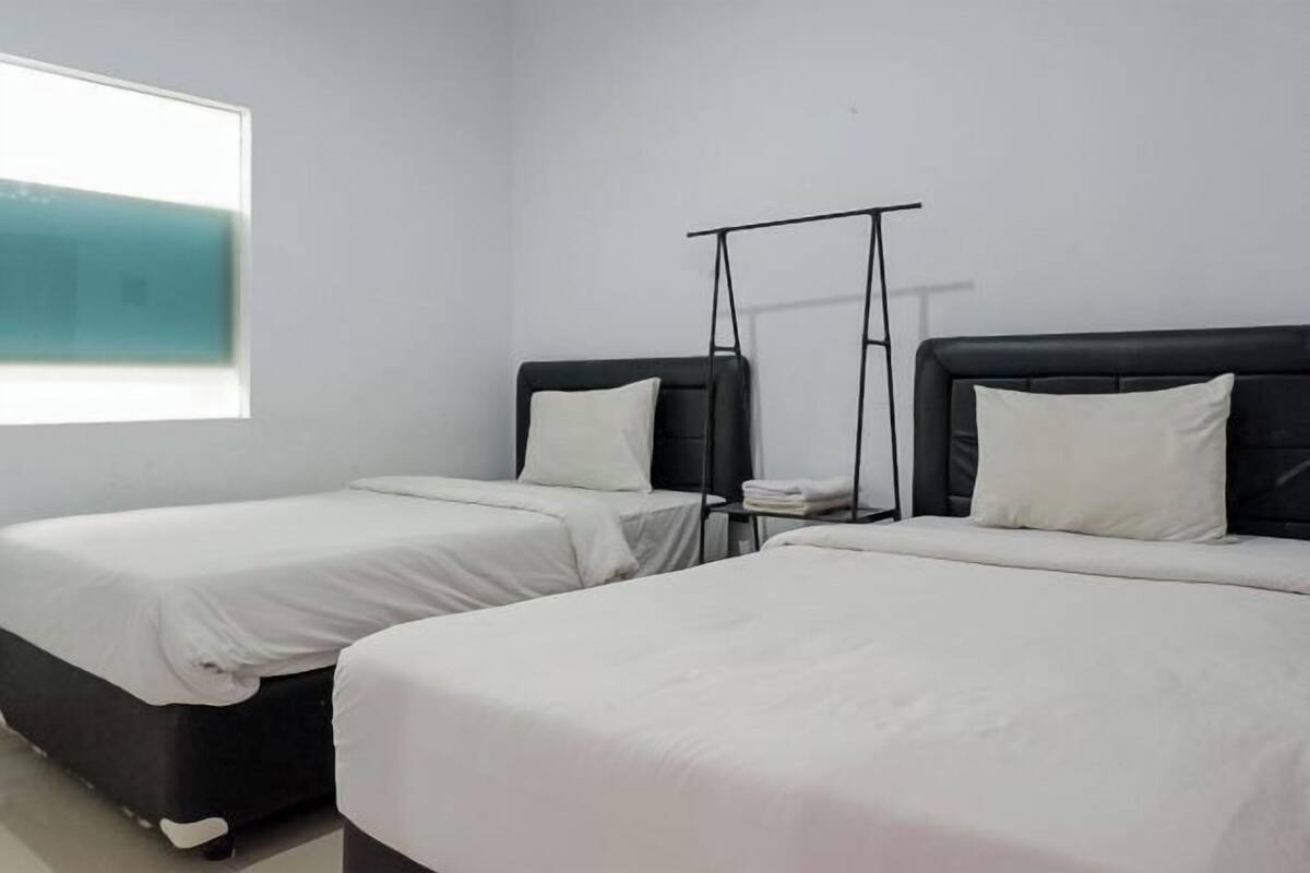 A hotel room with two single beds, a window, and a black metal rack.