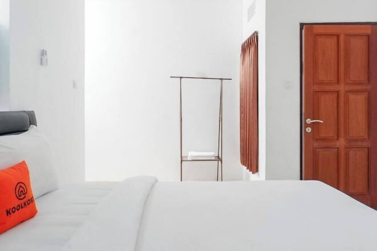 A hotel room with a bed, a metal shelf, a wooden door, and a white wall.