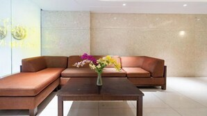 Eine moderne Lobby mit einem braunen Ecksofa, einem Holztisch und einem Blumenarrangement.