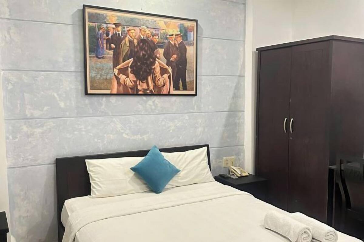 A hotel room with a bed, a nightstand, a framed painting, and a wardrobe.