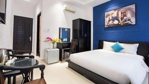 Ein Hotelzimmer mit Bett, Schreibtisch, Sessel, Fernseher und Bildern an der Wand.