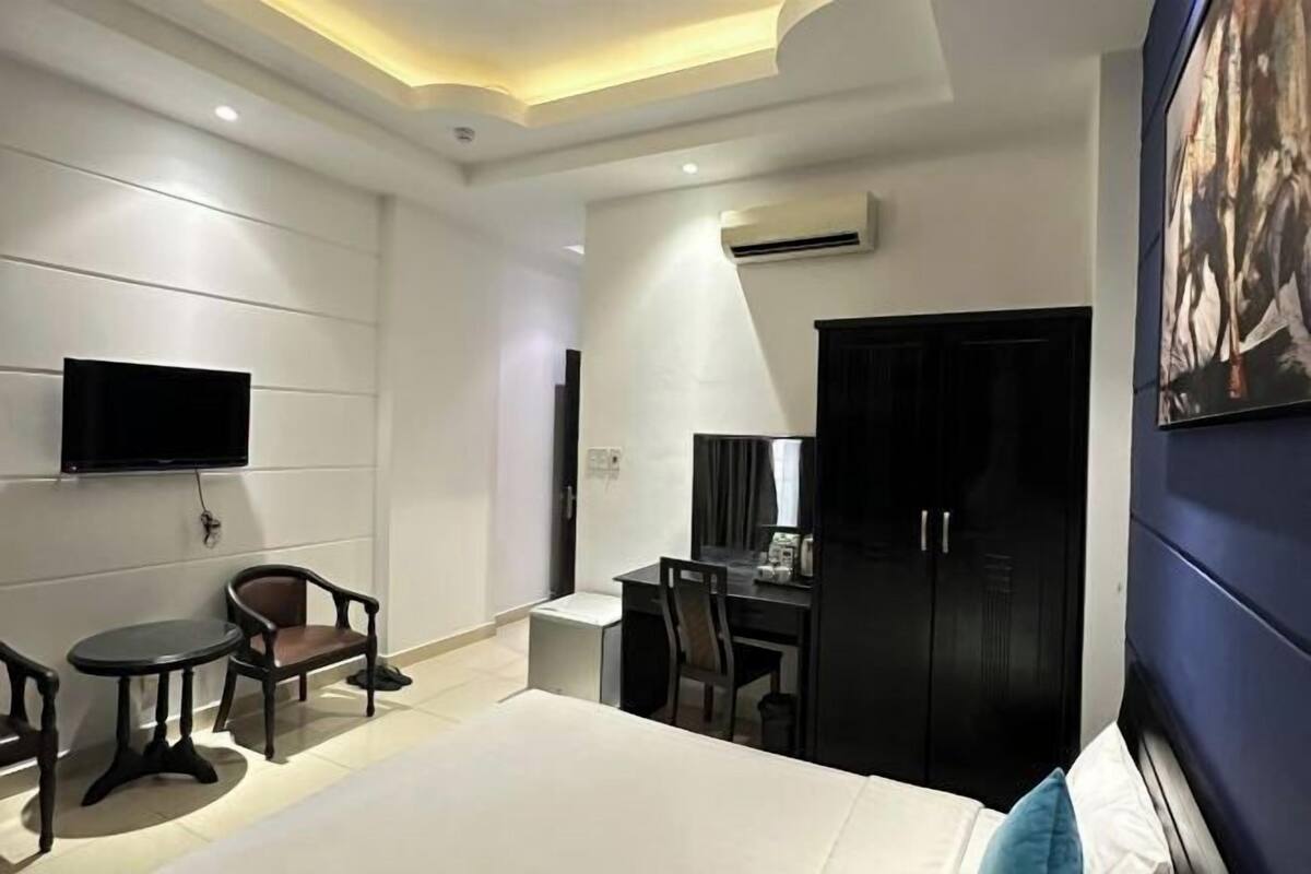 A modern hotel room with a bed, a desk, a chair, a TV, and a wardrobe.