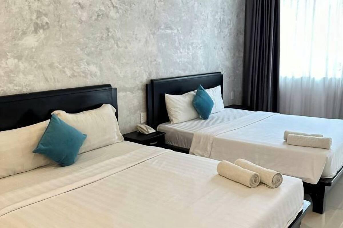A hotel room with two beds, each with a pillow and a rolled towel.