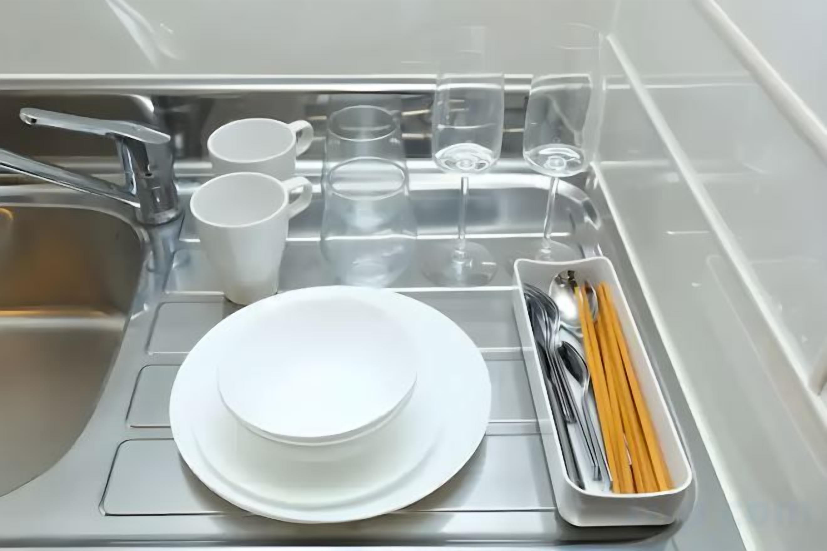A kitchen sink with stacked white plates, cups, and a utensil holder.