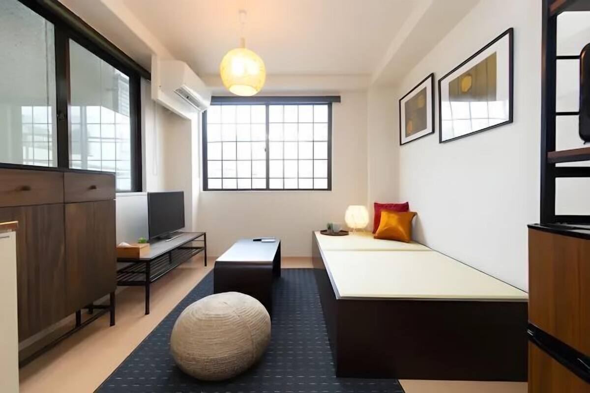 A modern hotel room with a large window, a flat-screen TV, a sofa, a small table, and a decorative lamp.