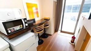 Una kitchenette equipada con microondas, un refrigerador pequeño, una mesa de comedor con sillas y un extintor.