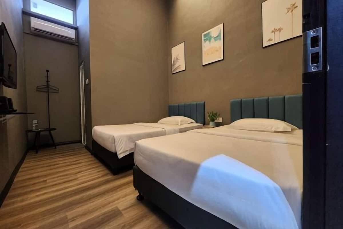 A hotel room with two beds, a wardrobe, a small table, and a window.