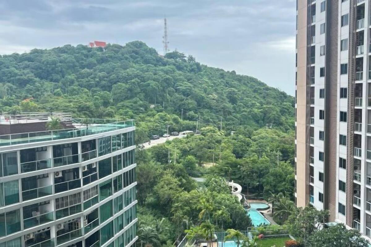 A high-rise building with a glass facade, a swimming pool, and lush greenery in the background.