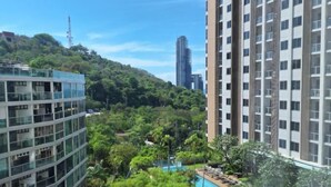 A modern building with a pool surrounded by lush greenery and a hill in the background. - unixx Seaview Resort (Pattaya)