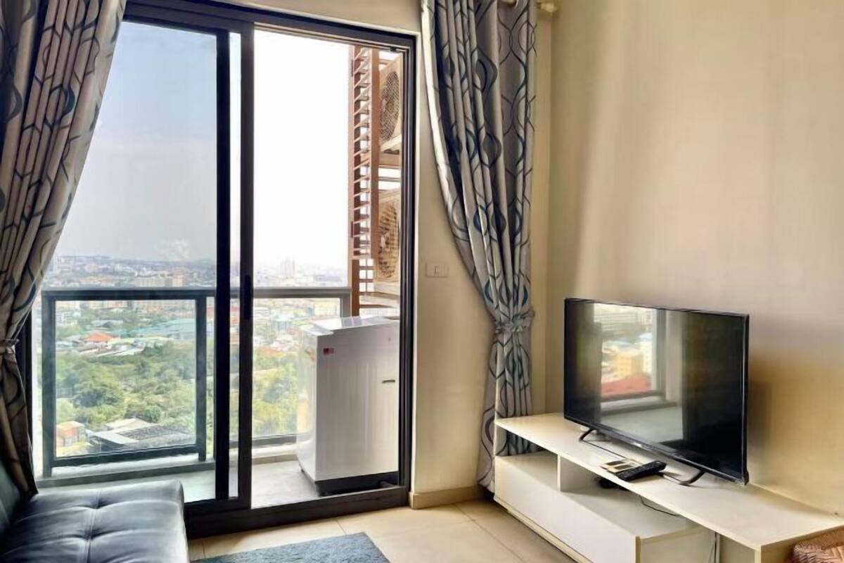 A modern living room with a large window, a flat-screen TV, a sofa, and a sliding glass door.