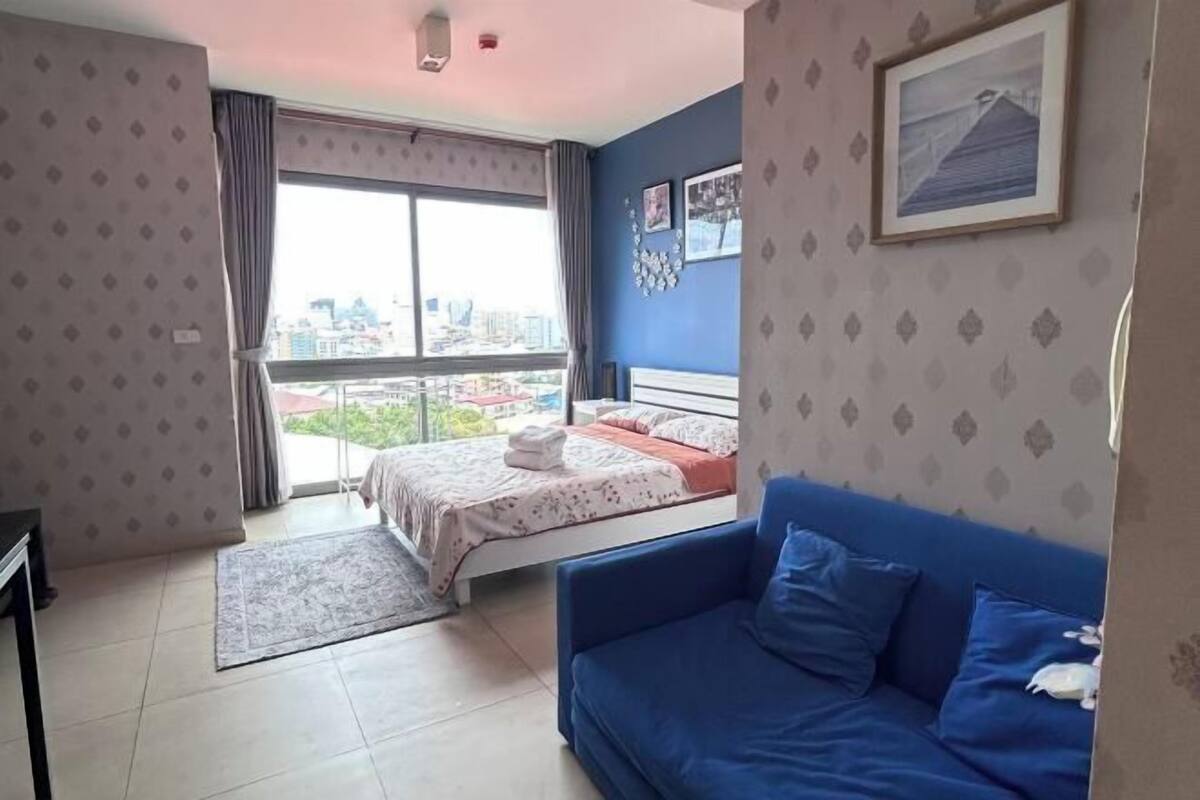A bedroom with a bed, a blue sofa, a window with curtains, and a city view.