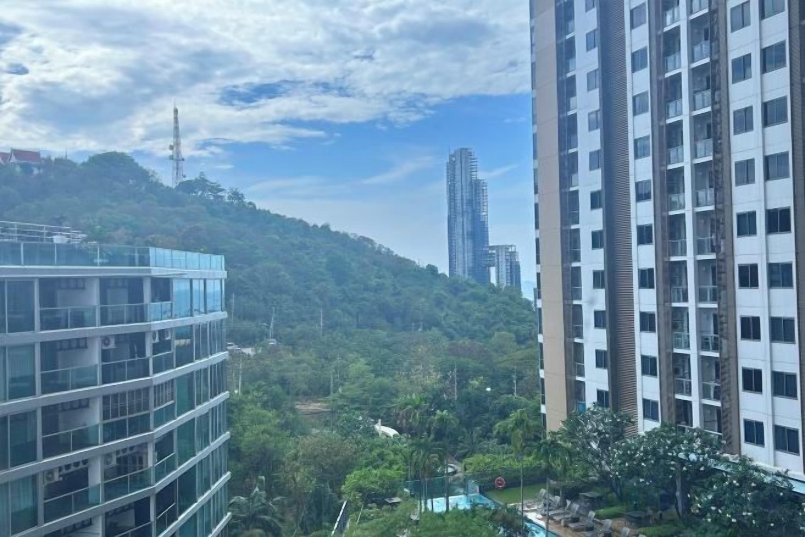 A high-rise building with a view of a lush green hill and a modern glass structure.