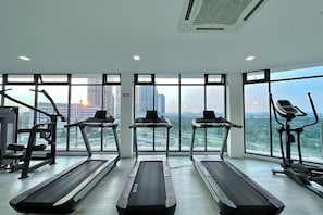 A gym with treadmills, a stationary bike, and weight machines. Large windows offer a city view. - Elysia Park Medini by Stayrene near Legoland (Iskandar Puteri)