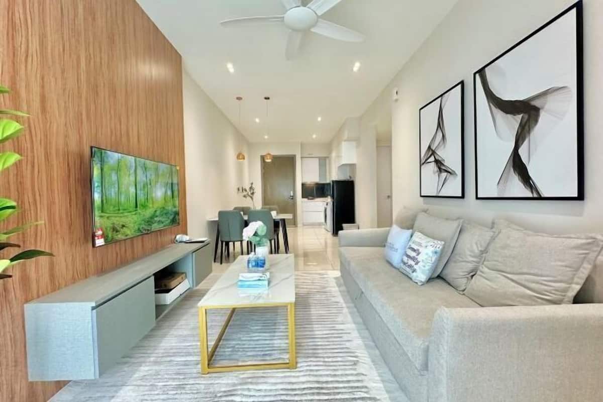 A modern living room with a sofa, coffee table, TV, artwork, and a dining area in the background.